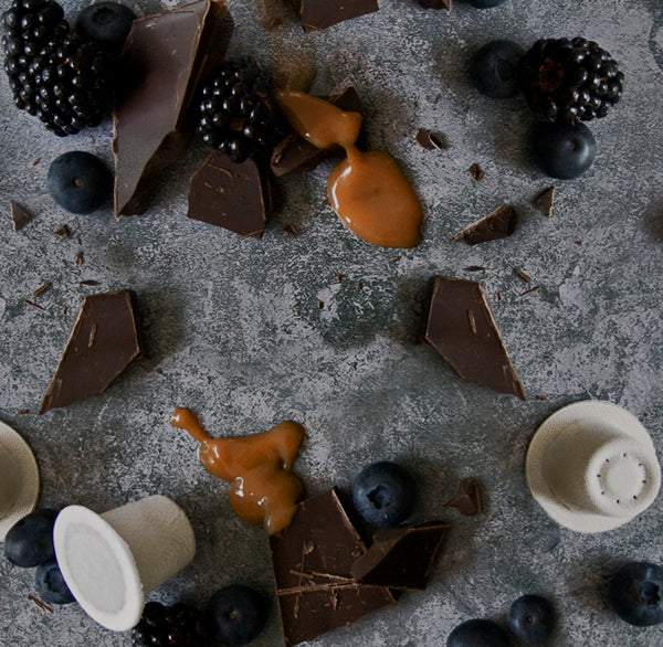 Ola home compostable coffee capsules on a table surrounded by chocolate and caramel